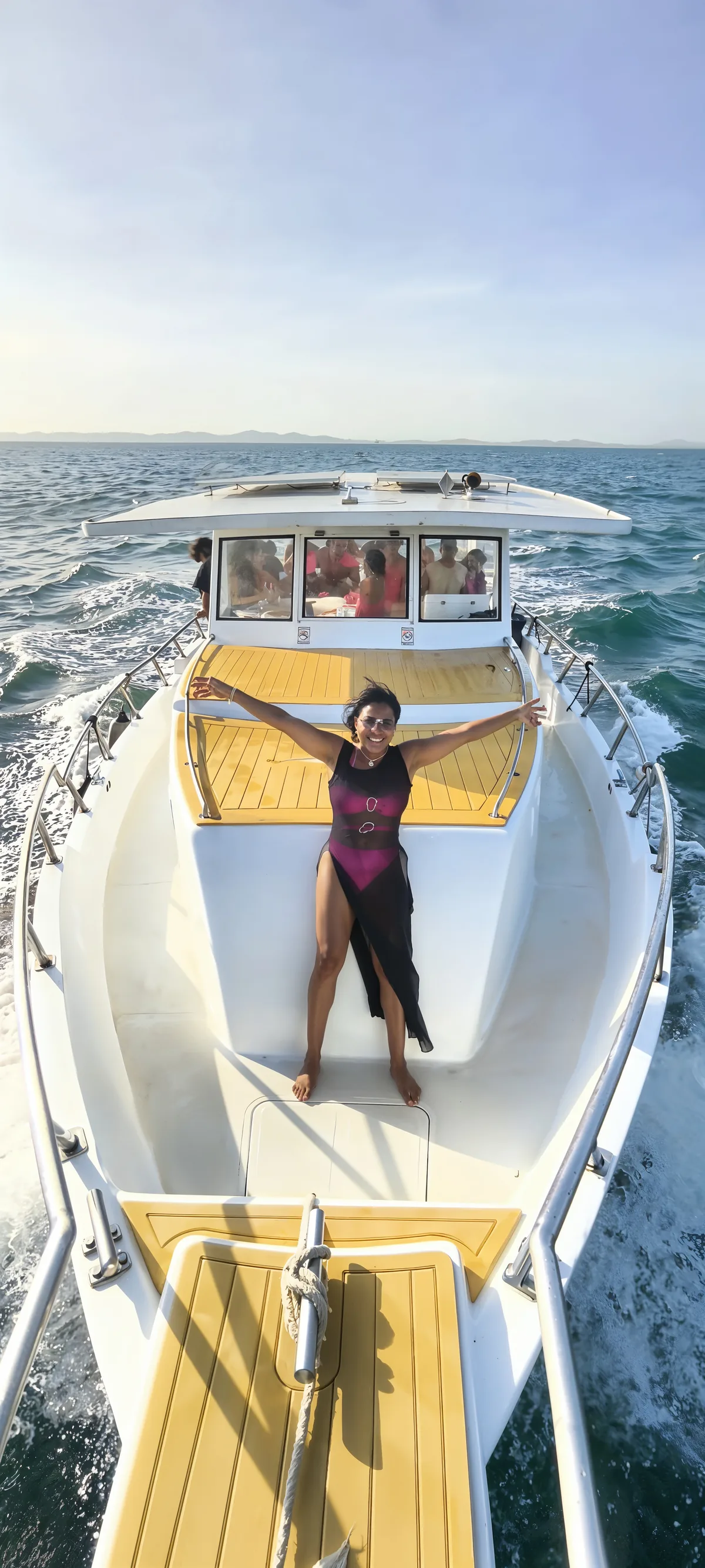 Cliente de braços abertos na proa da lancha da Acalma Alma navegando pelo mar de Salvador ao entardecer
